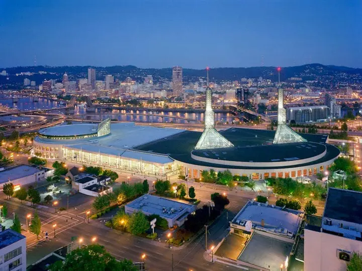 Aerial view of Portland cityscape and Oregon Convention Center at dusk with bright city lights reflecting in the river.