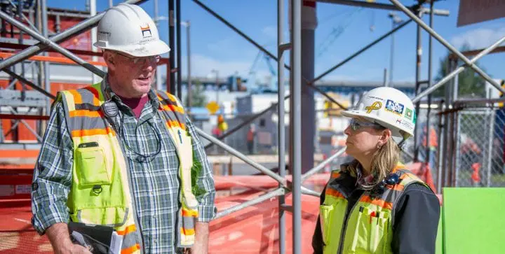 Construction workers in safety gear discussing plans at a building site on a sunny day.