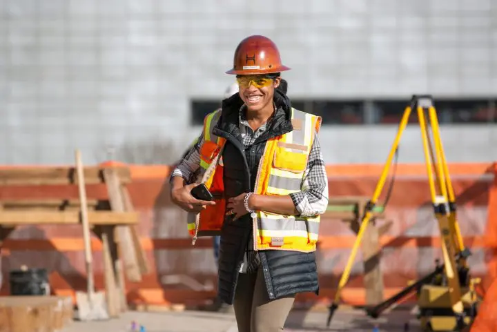 Smiling construction worker in safety gear and hard hat at a building site.