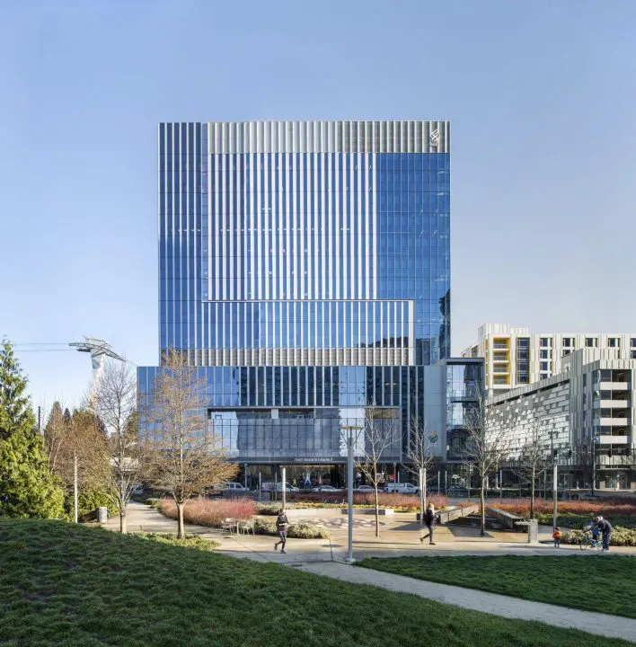 Modern glass office building with park and people walking in foreground on a clear day. Urban architecture and green space.