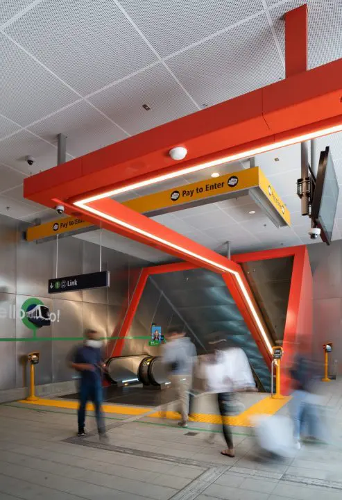Pedestrians passing a vibrant subway entrance with Pay to Enter signage, escalators, and modern design.