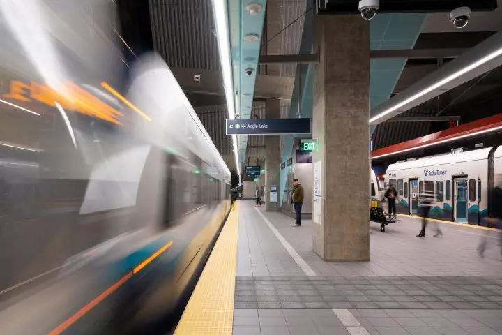 Modern subway station with a blurred train departing and people waiting on the platform, under a sign for Angle Lake station.