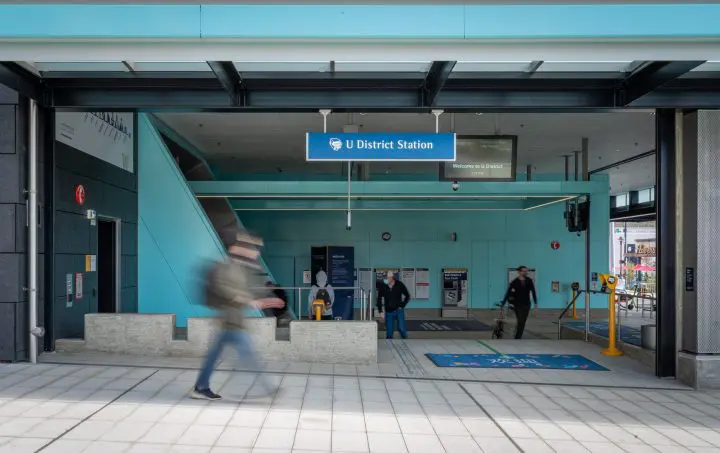 Modern U District Station entrance with people walking, turquoise decor, and directional signage for commuters.