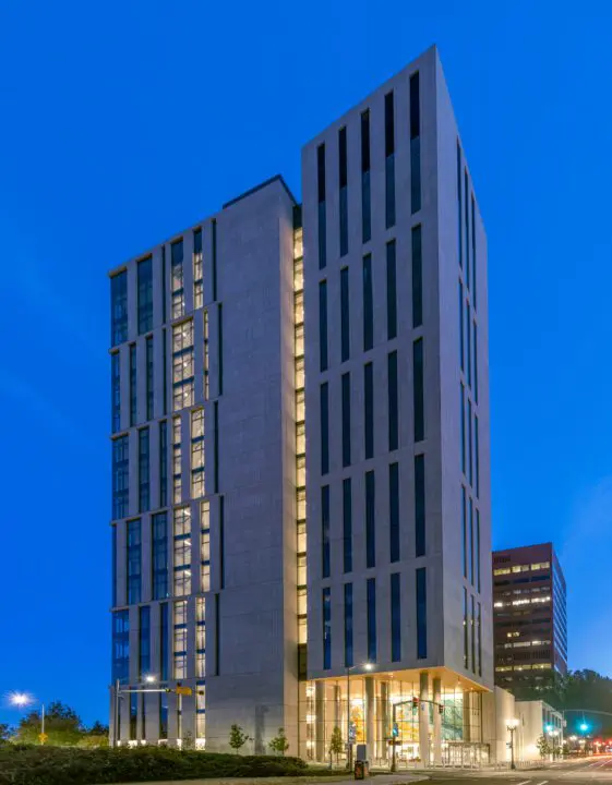 Modern high-rise building with illuminated windows at dusk, urban cityscape, clear blue sky background, street view.
