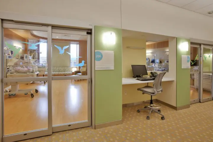 Modern hospital nursery room with incubators and computer station, featuring calming decor and natural light for newborn care.