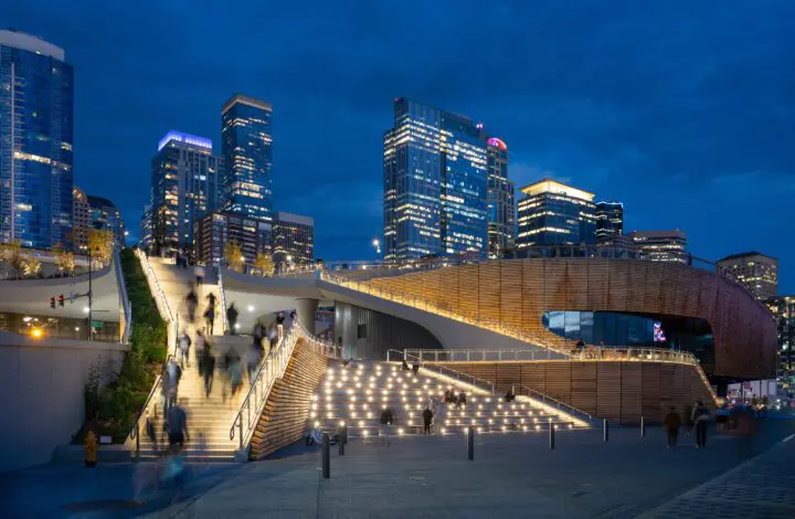 Modern urban architecture with illuminated stairs and people at dusk, set against a backdrop of high-rise city buildings.