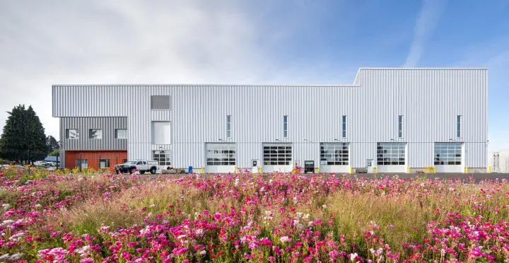 Modern industrial building with a colorful flower garden in the foreground under a clear sky.