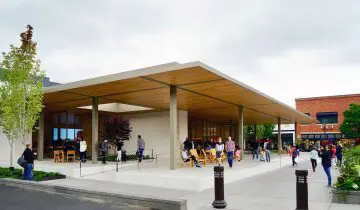 Modern architecture with people mingling outside an open, minimalist building. Lush greenery adds a touch of nature to the scene.