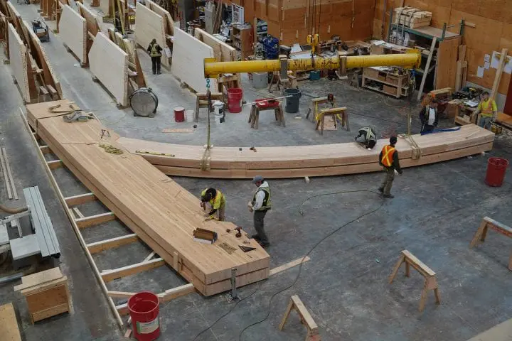 Workers assembling large wooden beams in a workshop, showcasing carpentry and construction process.