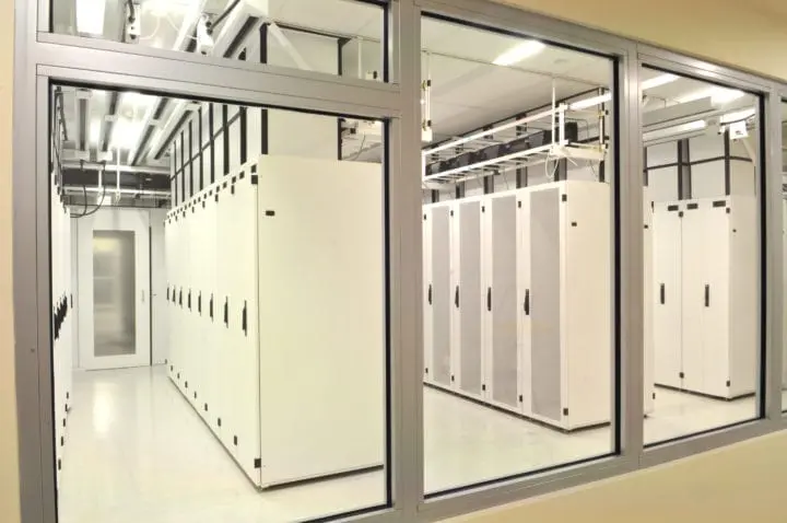 Bright data center with white server racks visible through glass walls, featuring secure storage and advanced technology infrastructure.