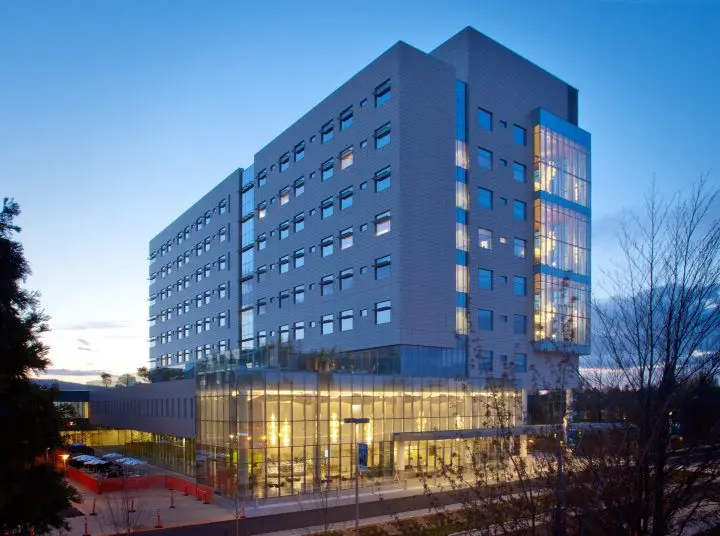 Modern office building with glass facade, illuminated at dusk, set against a clear evening sky.