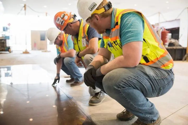 Construction workers in safety gear inspecting a polished floor indoors.