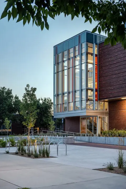Modern building with glass facade, surrounded by trees and bike racks, under a clear sky.