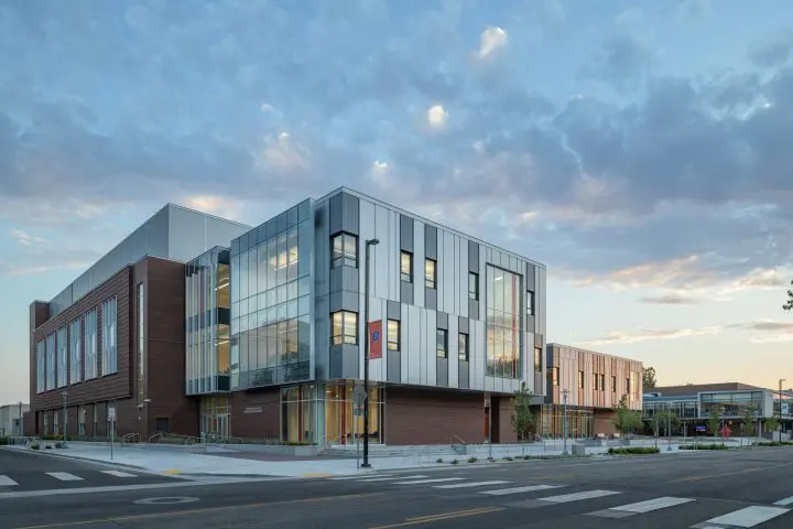 Modern academic building with sleek glass facade and brick accents under a vibrant sky at sunset.