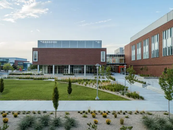 Modern educational campus with brick buildings, green lawn, and pathways under a clear sky.