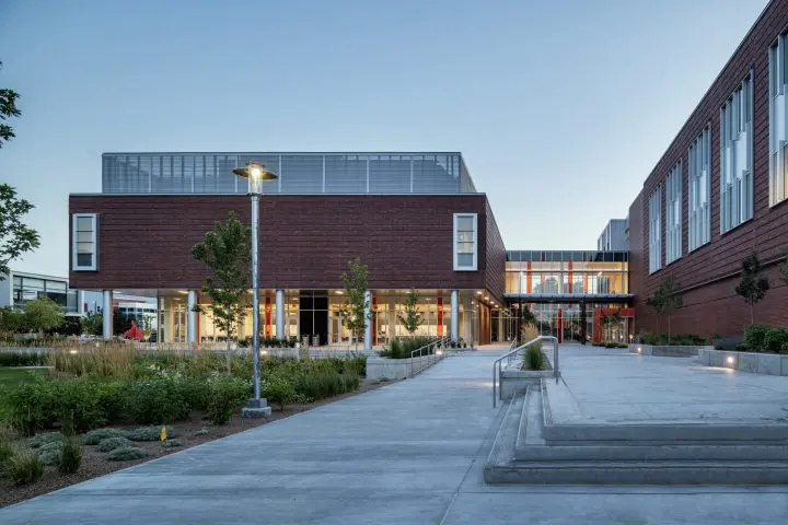Contemporary brick building exterior with greenery, illuminated at dusk, featuring skyward view and modern architecture.