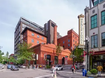 Historic red brick building with Whole Foods sign in urban setting, pedestrians crossing and cars parked nearby.