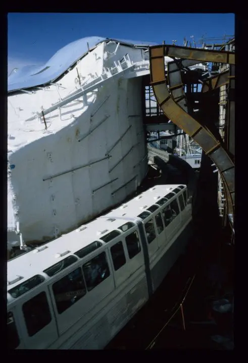 Monorail passing through unique architectural structure under blue sky; urban transportation meets modern design.