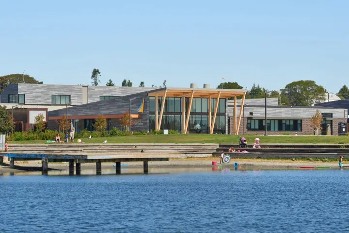Modern building by a lake with people enjoying the sunny day in the park.