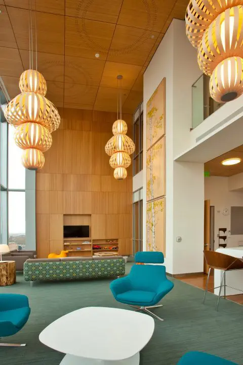 Modern lounge with teal chairs, wooden accents, and unique pendant lights, creating a warm, inviting atmosphere.