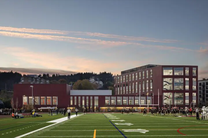 Modern school building at sunset with sports field and people, highlighting education and community activities.
