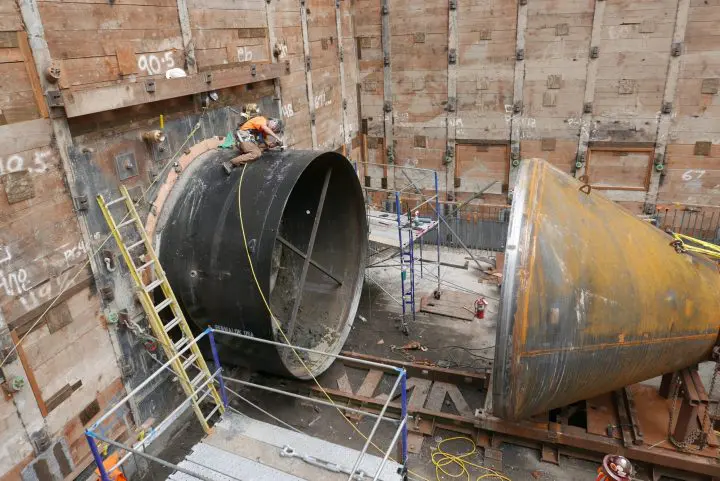 Engineer working on large tunnel pipe connection at construction site, surrounded by scaffolding and equipment.
