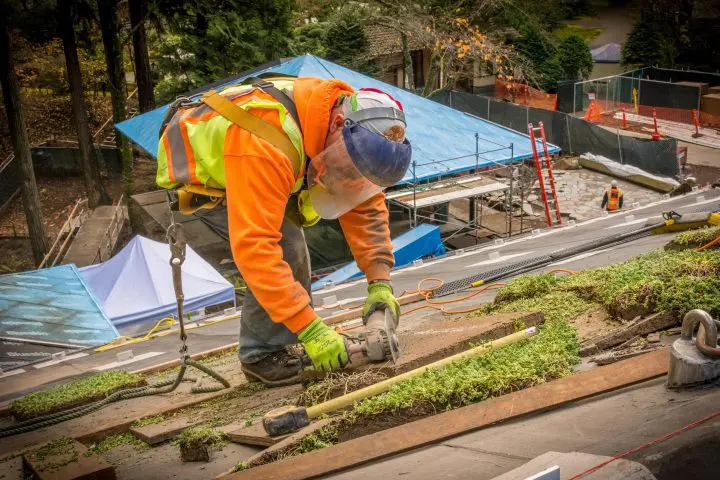 Construction worker with safety gear using tools on a green roof installation.