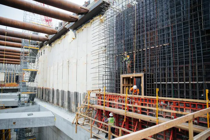 Construction workers building reinforced concrete structure with scaffolding and safety gear. Large-scale industrial project underway.