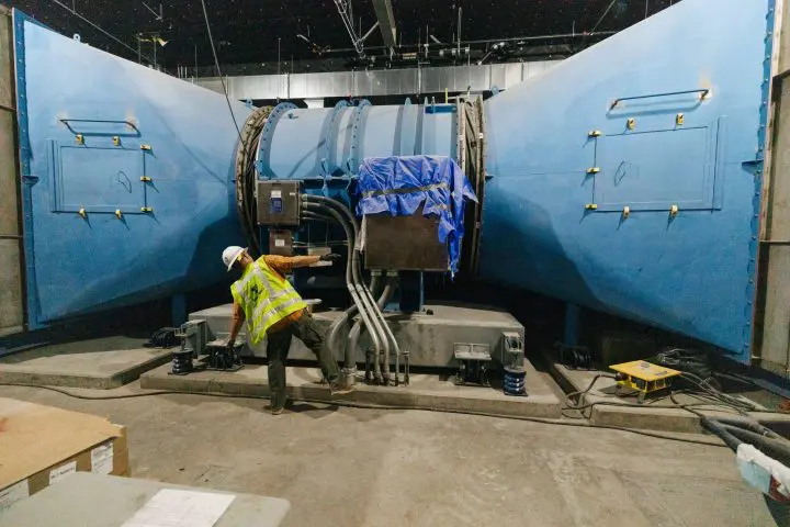 Worker in hard hat and vest inspecting large industrial equipment in a facility.
