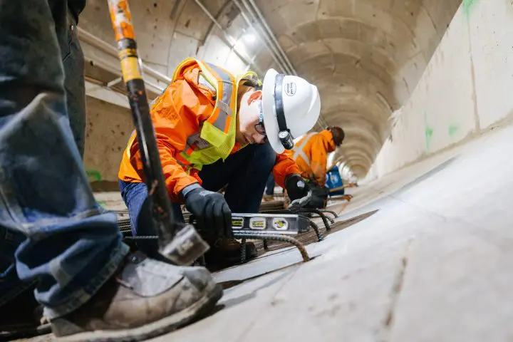 Construction workers in a tunnel, wearing safety gear, measuring rebar for reinforcement.