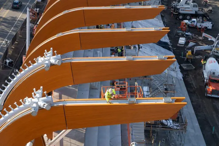 Aerial view of construction worker on curved wooden beams, busy building a modern structure at a construction site with machinery.