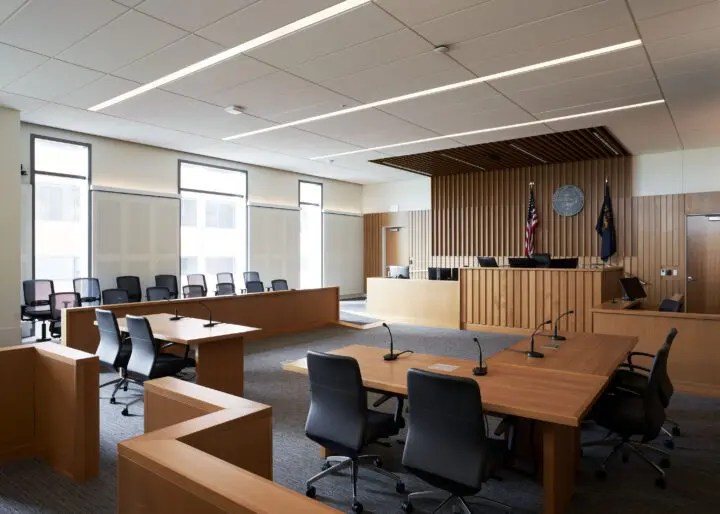 Modern courtroom with wooden furniture, empty seating, and flags on display, conveying justice and legal proceedings ambiance.