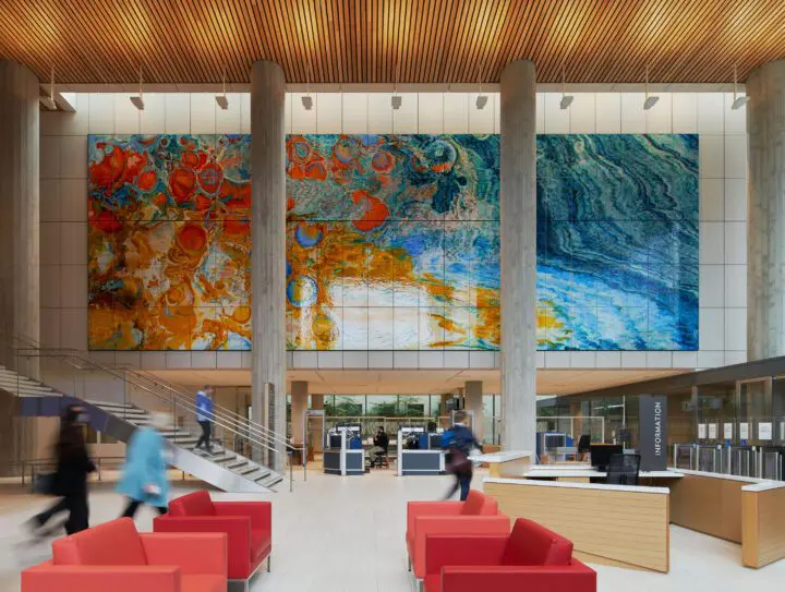 Modern lobby with vibrant abstract wall art, red chairs, and people moving through the space.
