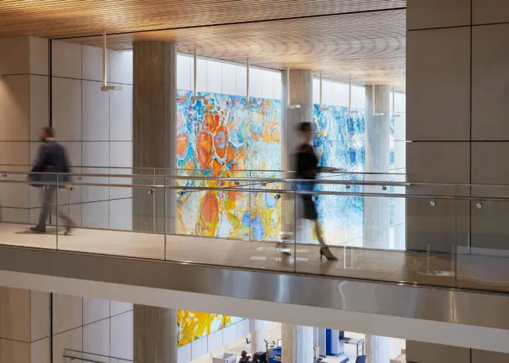 Modern office interior with artistic wall panels, people walking on a glass walkway, showcasing corporate art and design.