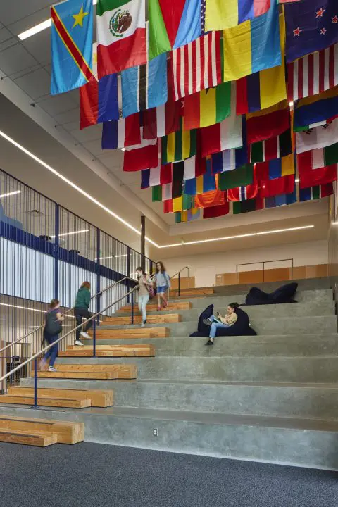 Modern interior with international flags, staircase seating, and people engaging in activities, fostering a diverse and inclusive space.