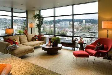 Modern living room with large windows, city view, cozy seating, colorful cushions, vibrant decor, and natural light.