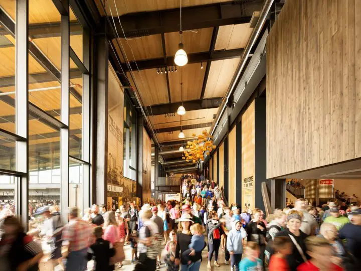 Bustling crowd in modern indoor marketplace with wooden walls and high ceiling, large windows letting in natural light.
