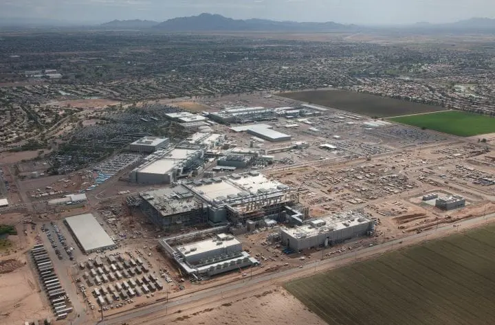 Aerial view of a large industrial complex in a sprawling desert landscape with surrounding fields and mountains in the distance.
