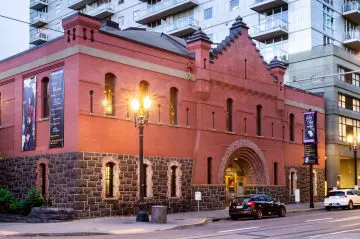 Historic red-brick building with arched entrance and city street view at dusk, featuring cars and lampposts nearby.