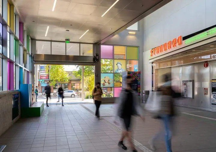 Pedestrians walk through a brightly colored urban corridor featuring modern architecture and a storefront.