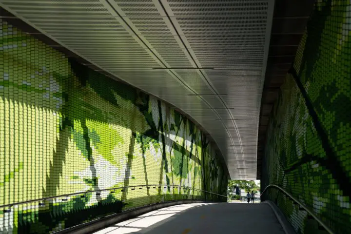 Futuristic walkway with green mosaic walls and sunlight casting patterns, leading to two figures in the distance.