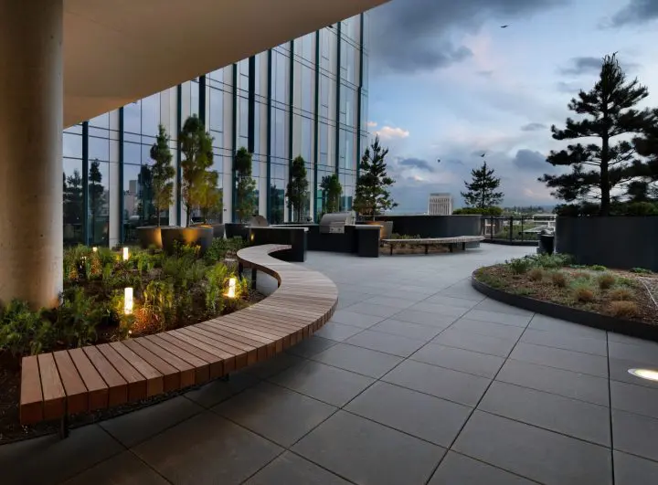 Modern rooftop garden with wooden benches, plants, and skyline view under a cloudy sky.
