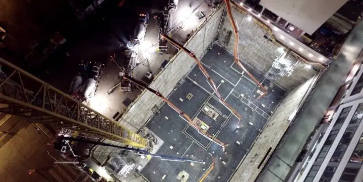 Overhead view of a nighttime construction site with cranes and concrete mixers working in a large excavation pit.