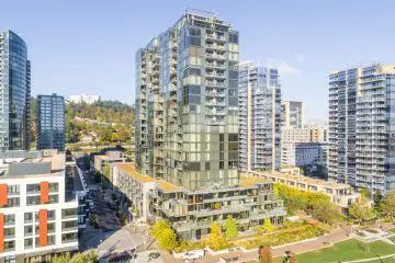 Aerial view of modern city apartments with greenery, showcasing urban architecture against a backdrop of hills and clear sky.