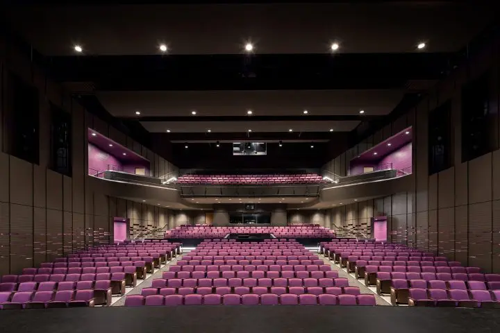Modern theater with purple seats, multiple balconies, and stage view. Elegant lighting and design for performances or events.
