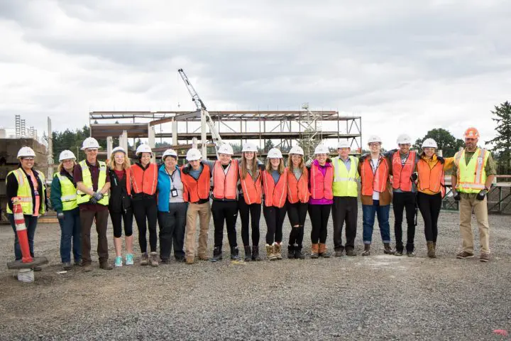 Diverse group of construction workers in safety gear standing on site, with a building framework in the background.