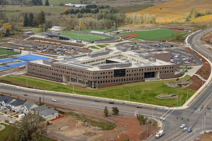 Aerial view of a modern school campus with sports fields, parking, and surrounding roads in a scenic countryside setting.