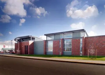 Modern brick and metal building under blue sky with clouds, viewed from a street perspective.