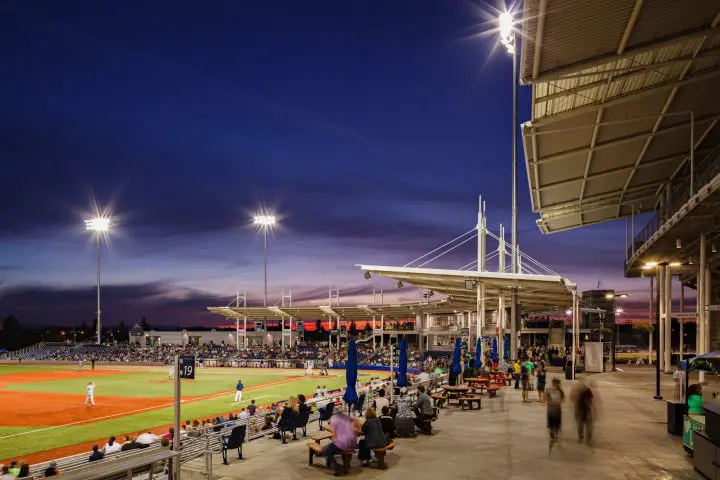 Twilight baseball game at a bustling stadium with a vibrant sky, illuminating lights, and fans engaged in the action.
