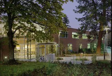 Modern brick building at dusk surrounded by trees, with a bike parked near the entrance.
